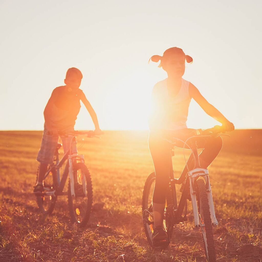 Enfants qui font du vélo au coucher de soleil dans un champs